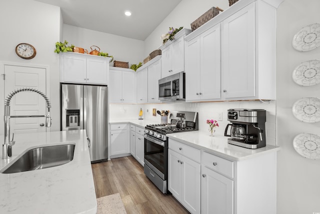 kitchen with white cabinets, appliances with stainless steel finishes, a sink, light wood-type flooring, and backsplash