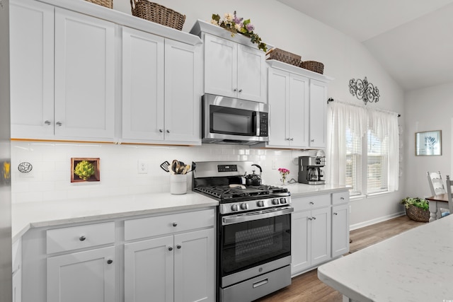 kitchen featuring tasteful backsplash, white cabinets, appliances with stainless steel finishes, vaulted ceiling, and light wood-type flooring