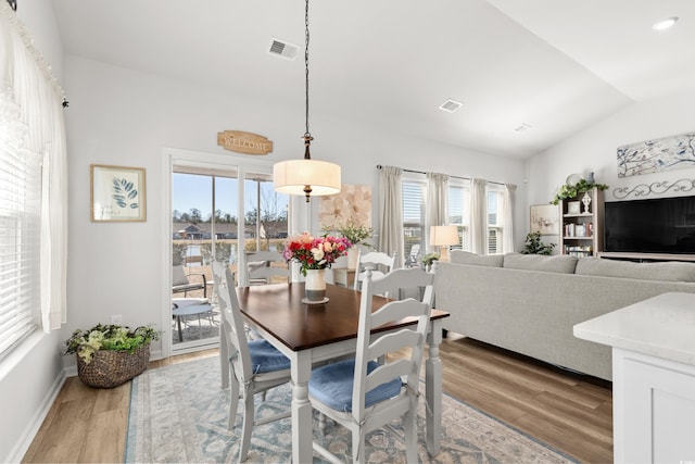 dining space with light wood-type flooring, visible vents, and vaulted ceiling