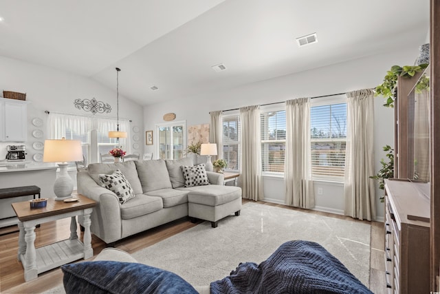 living area featuring lofted ceiling, light wood finished floors, baseboards, and visible vents