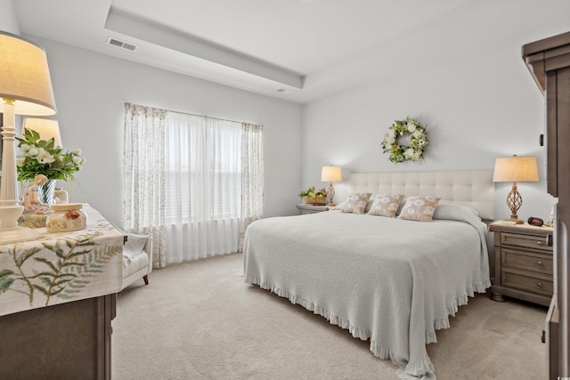 bedroom featuring light carpet, visible vents, and a tray ceiling