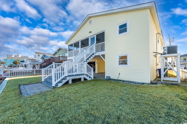 back of property with ceiling fan, a yard, stairway, and a sunroom