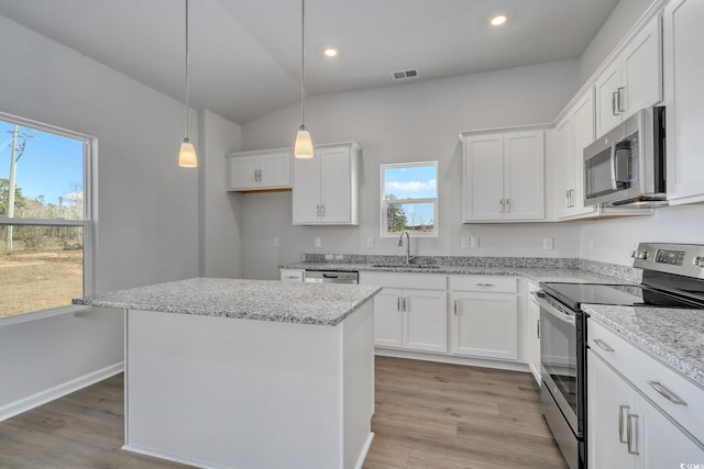 kitchen featuring light wood finished floors, stainless steel appliances, white cabinets, a sink, and a kitchen island