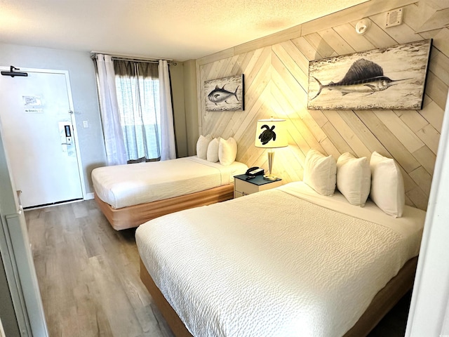 bedroom featuring wood walls, a textured ceiling, and wood finished floors