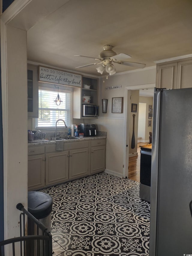 kitchen with a ceiling fan, wainscoting, tile patterned flooring, stainless steel appliances, and a sink