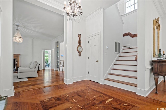 foyer entrance featuring ornamental molding, visible vents, and an inviting chandelier