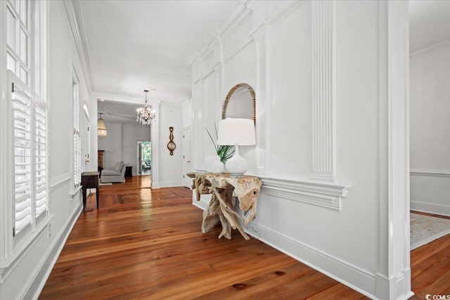 corridor featuring baseboards, an inviting chandelier, hardwood / wood-style flooring, and crown molding