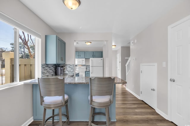 kitchen with backsplash, blue cabinetry, dark wood finished floors, a peninsula, and white appliances