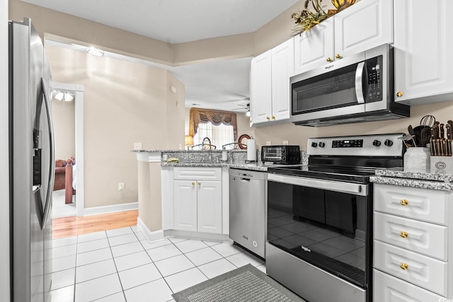 kitchen featuring light stone counters, a peninsula, stainless steel appliances, white cabinetry, and light tile patterned flooring