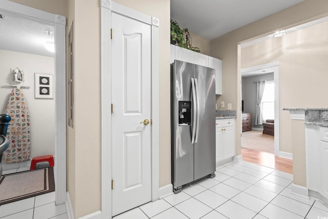 kitchen featuring light stone counters, stainless steel refrigerator with ice dispenser, light tile patterned flooring, and white cabinets