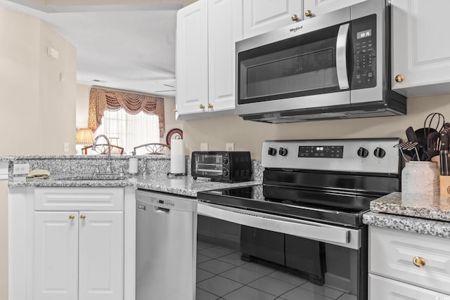 kitchen featuring a toaster, appliances with stainless steel finishes, a peninsula, white cabinetry, and a sink