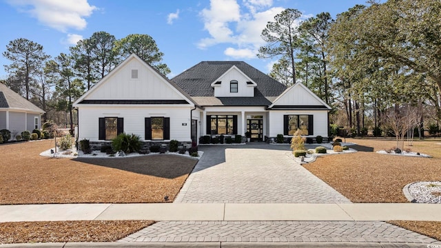 modern farmhouse featuring decorative driveway, roof with shingles, board and batten siding, a standing seam roof, and metal roof