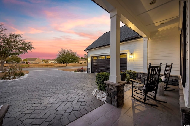 patio terrace at dusk with decorative driveway and an attached garage