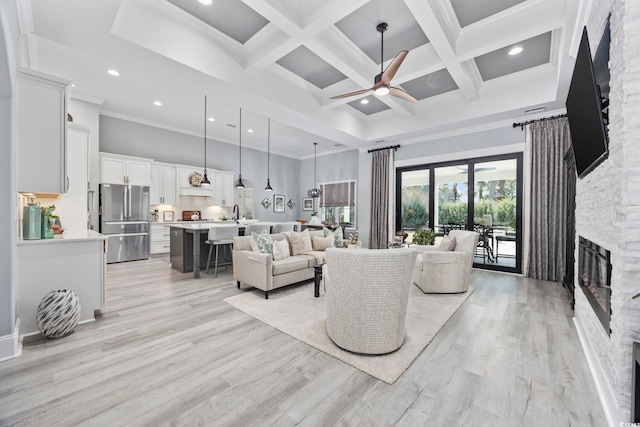 living area featuring light wood-style flooring, a fireplace, coffered ceiling, a towering ceiling, and beamed ceiling