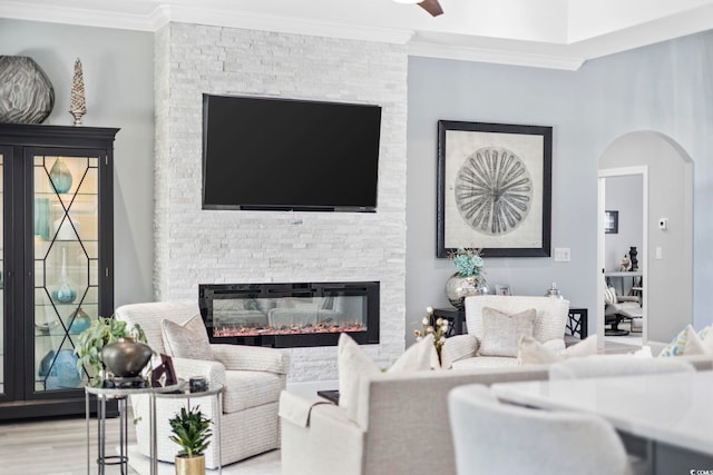 living area with arched walkways, a stone fireplace, wood finished floors, and crown molding