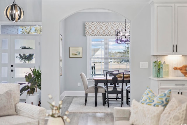 dining area with arched walkways, a notable chandelier, baseboards, and wood finished floors