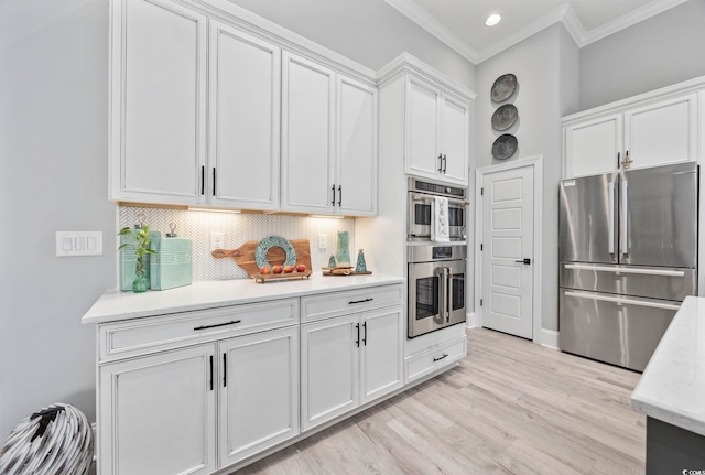 kitchen with light wood finished floors, stainless steel appliances, decorative backsplash, ornamental molding, and white cabinets