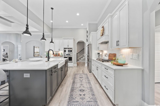 kitchen featuring arched walkways, stainless steel appliances, gray cabinets, white cabinetry, and a sink