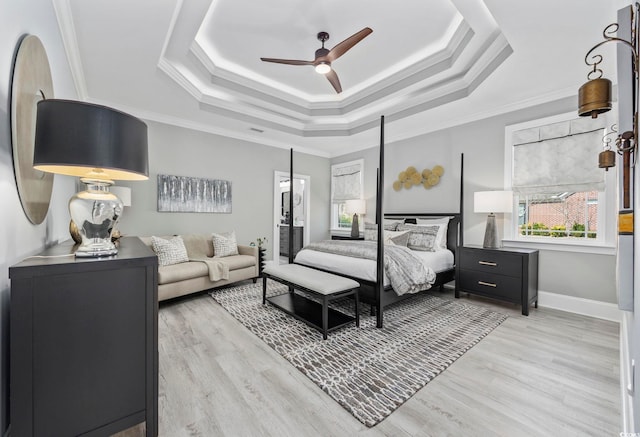 bedroom featuring light wood-style floors, a raised ceiling, crown molding, and baseboards