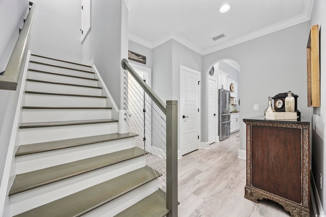 staircase with arched walkways, wood finished floors, visible vents, and crown molding