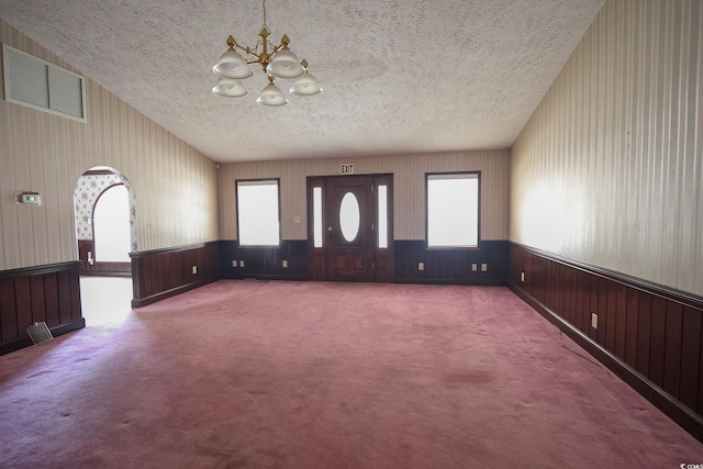 interior space with visible vents, arched walkways, a wainscoted wall, an inviting chandelier, and a textured ceiling