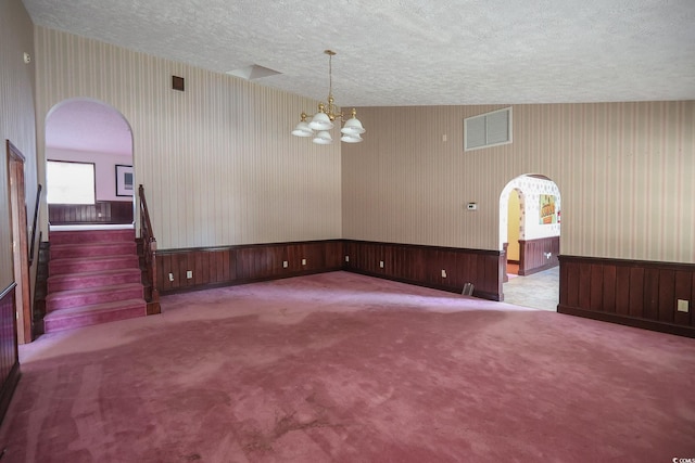 carpeted spare room with arched walkways, wainscoting, visible vents, and wallpapered walls