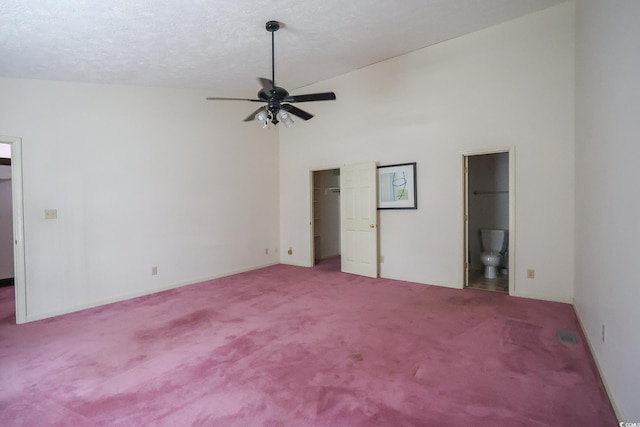 unfurnished bedroom featuring connected bathroom, carpet, a walk in closet, a textured ceiling, and high vaulted ceiling