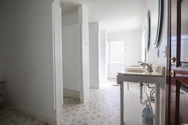 bathroom featuring a textured ceiling, a sink, and baseboards