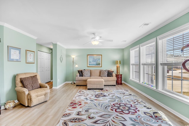 living area featuring baseboards, visible vents, light wood-style flooring, ceiling fan, and crown molding