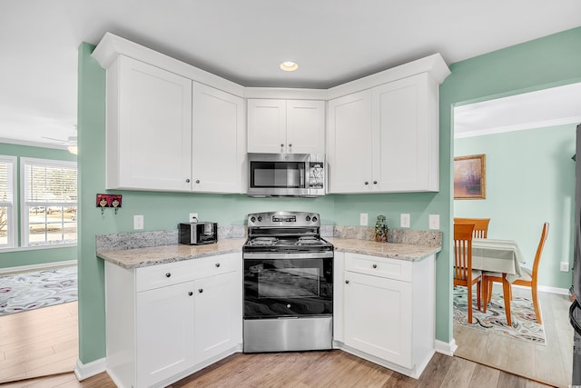 kitchen featuring baseboards, white cabinets, light wood-style flooring, appliances with stainless steel finishes, and light stone countertops