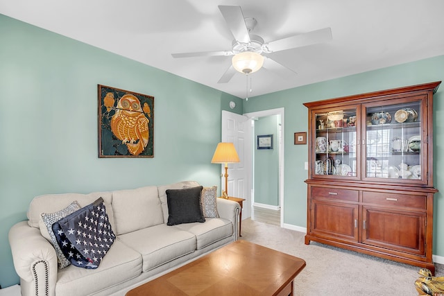 living area with light carpet, a ceiling fan, and baseboards