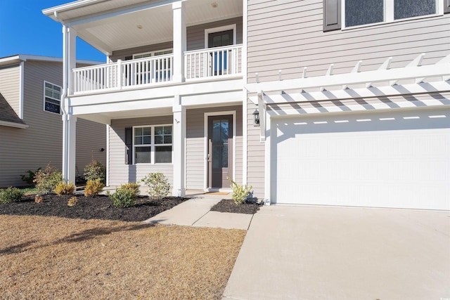 doorway to property with a balcony, an attached garage, and concrete driveway