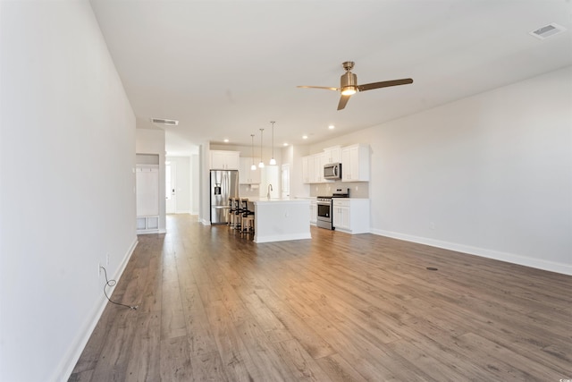 unfurnished living room featuring baseboards, visible vents, ceiling fan, and wood finished floors