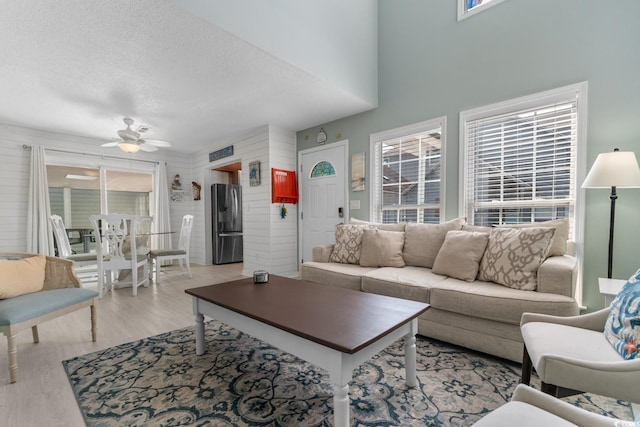 living area featuring light wood-style floors, a ceiling fan, and a textured ceiling