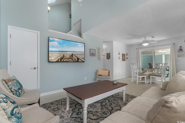 living area with a high ceiling, ceiling fan, a textured ceiling, wood finished floors, and baseboards