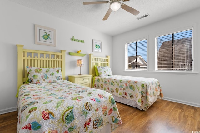 bedroom with baseboards, visible vents, a ceiling fan, wood finished floors, and a textured ceiling