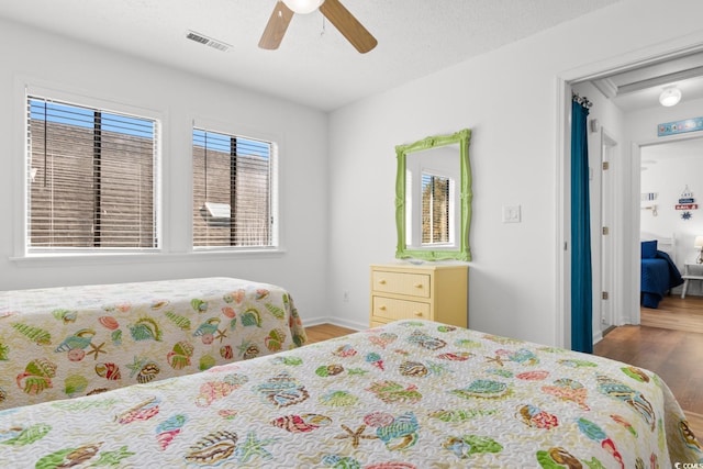 bedroom with a ceiling fan, a textured ceiling, visible vents, and wood finished floors