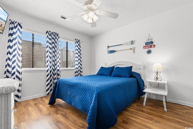 bedroom featuring ceiling fan, a textured ceiling, wood finished floors, visible vents, and baseboards