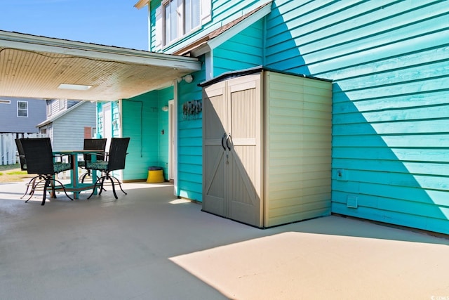 view of patio with outdoor dining space, an outdoor structure, fence, and a storage unit