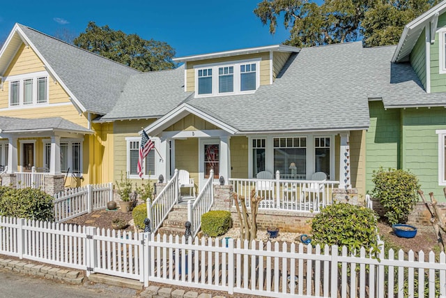 view of front of house with a shingled roof, covered porch, and a fenced front yard