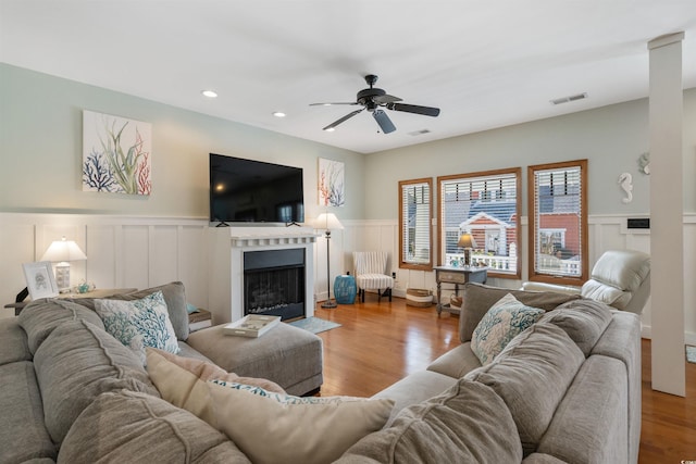 living room with visible vents, wood finished floors, a fireplace with flush hearth, and a ceiling fan