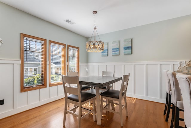 dining area with visible vents, wainscoting, light wood-type flooring, a chandelier, and a decorative wall