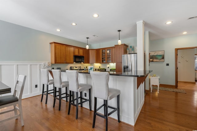 kitchen with a breakfast bar area, stainless steel appliances, wood finished floors, brown cabinetry, and glass insert cabinets