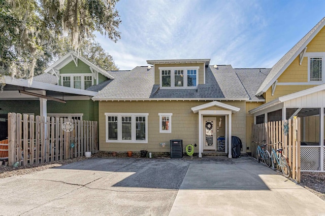 view of front facade with a shingled roof, central AC, and fence