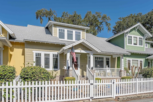 view of front of house featuring a porch, roof with shingles, and a fenced front yard