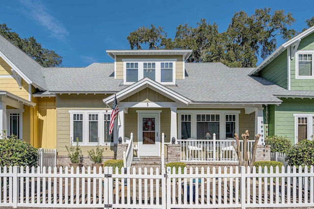 view of front of home with covered porch, a shingled roof, a fenced front yard, and board and batten siding