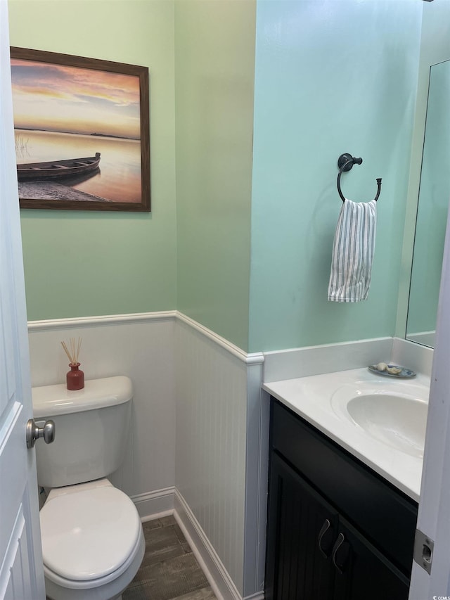 half bath featuring wainscoting, vanity, toilet, and wood finished floors