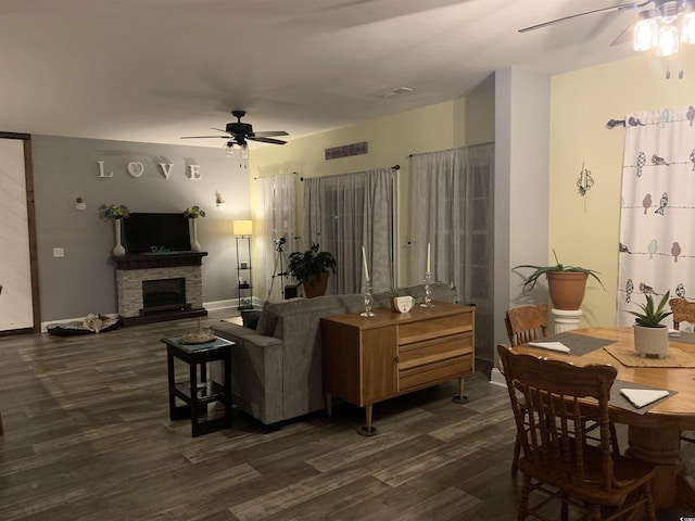 living area with a ceiling fan, visible vents, baseboards, dark wood-style flooring, and a stone fireplace