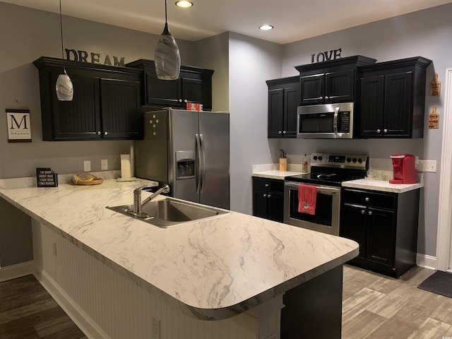 kitchen featuring a peninsula, dark cabinets, appliances with stainless steel finishes, and a sink