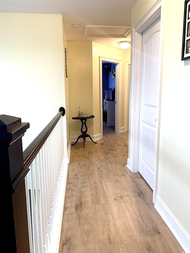 hall with an upstairs landing, light wood finished floors, attic access, and baseboards